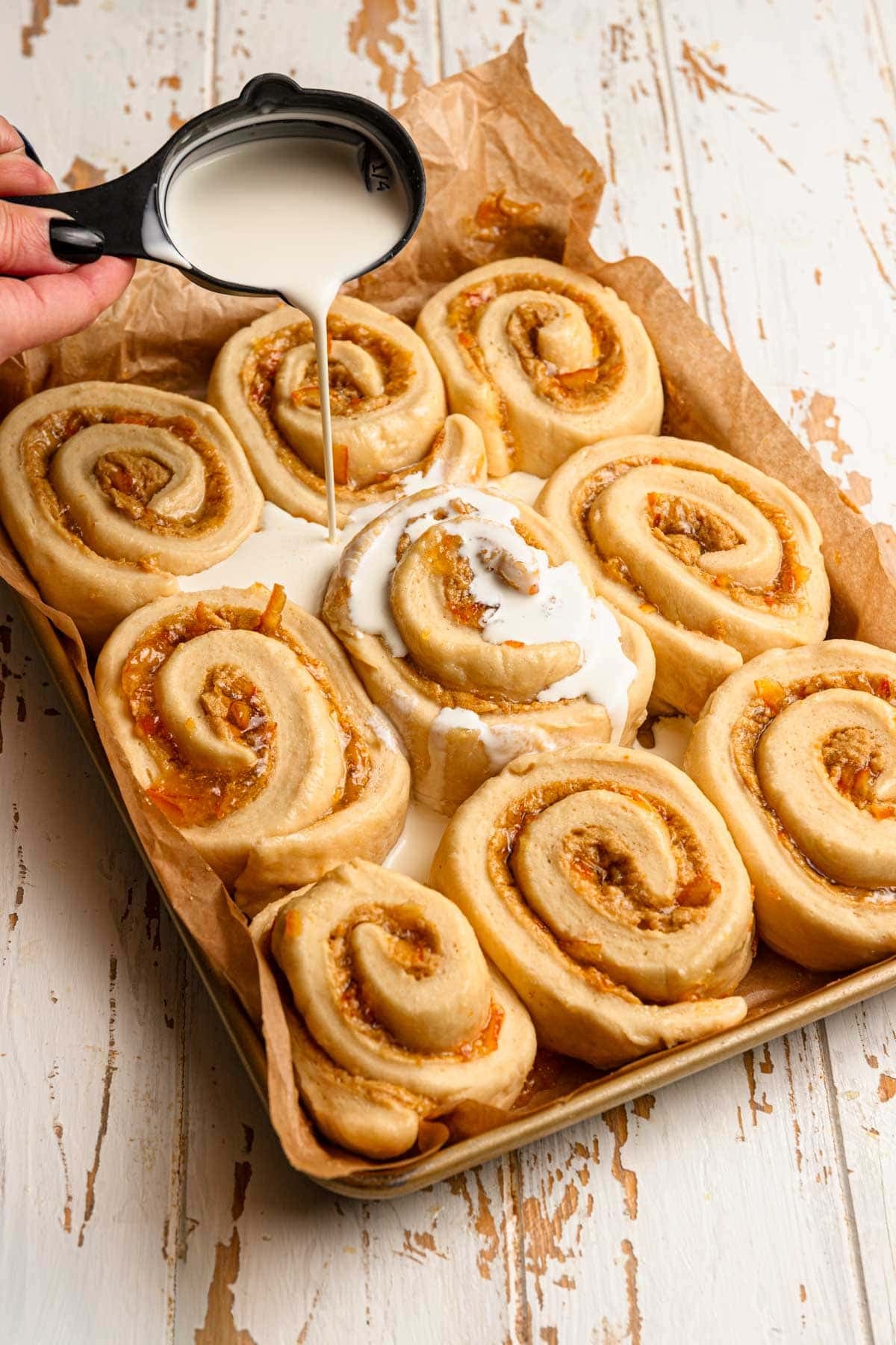 Pouring cream over a pan with unbaked orange rolls.
