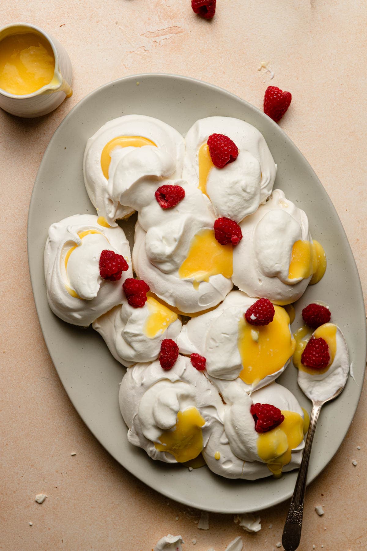 a plate with mini pull apart pavlovas topped with lemon curd, cream and fresh raspberries.