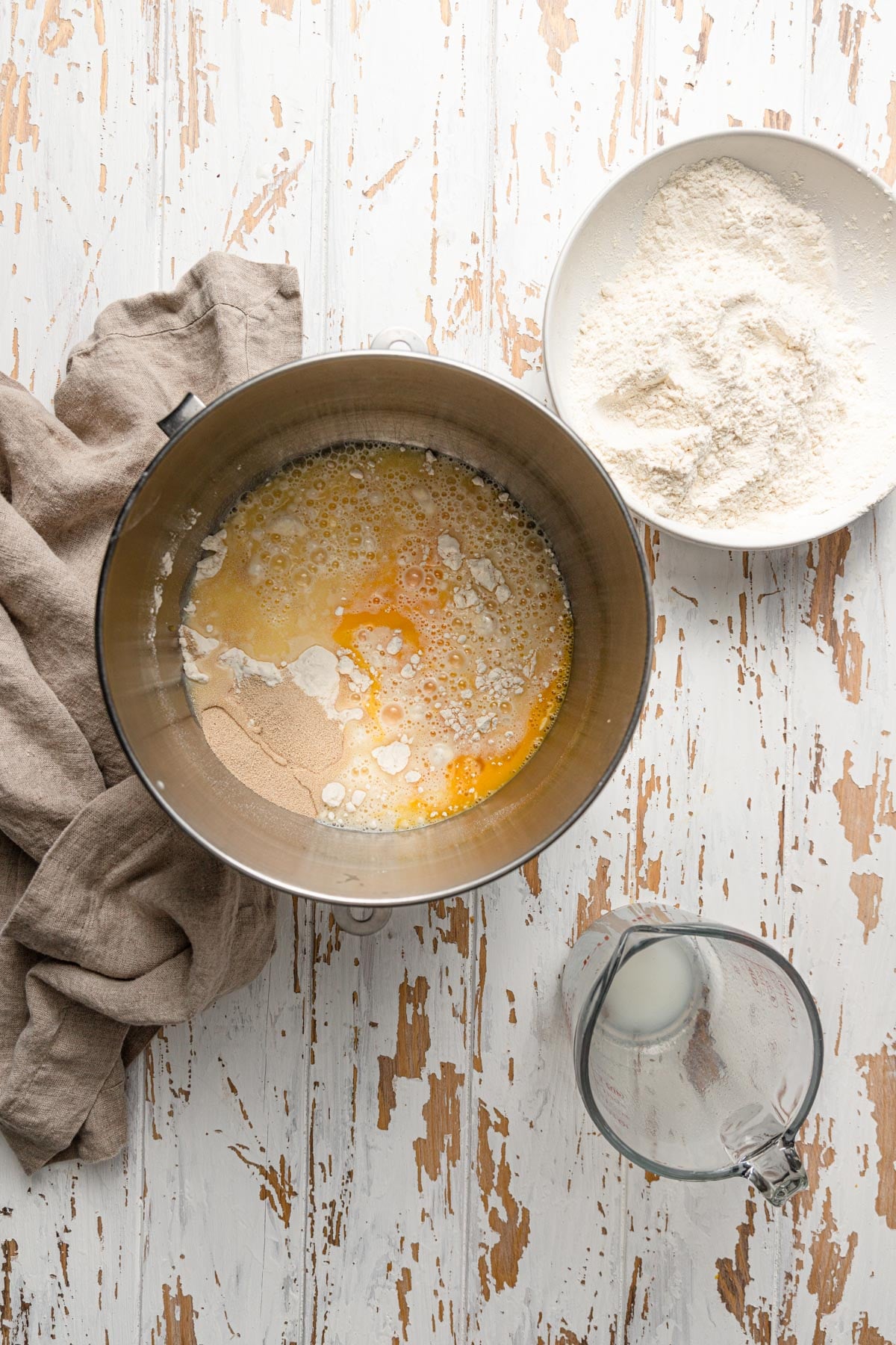 A bowl of a stand mixer with milk, flour, eggs and yeast. 