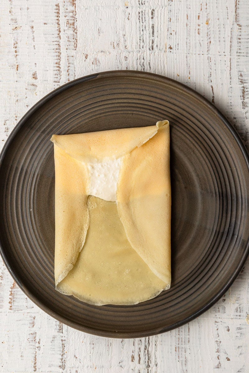 A plate topped with crepe topped with cheese filling, sides are folded.
