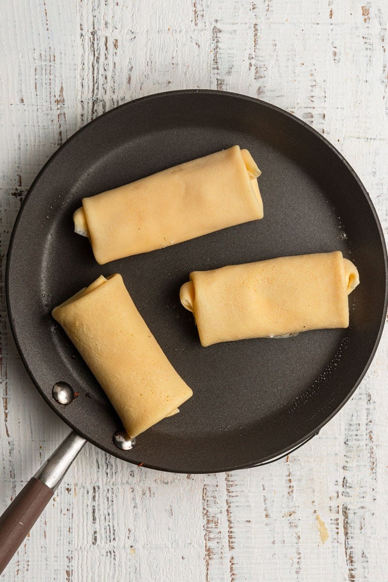 A skillet with three rolled crepes.