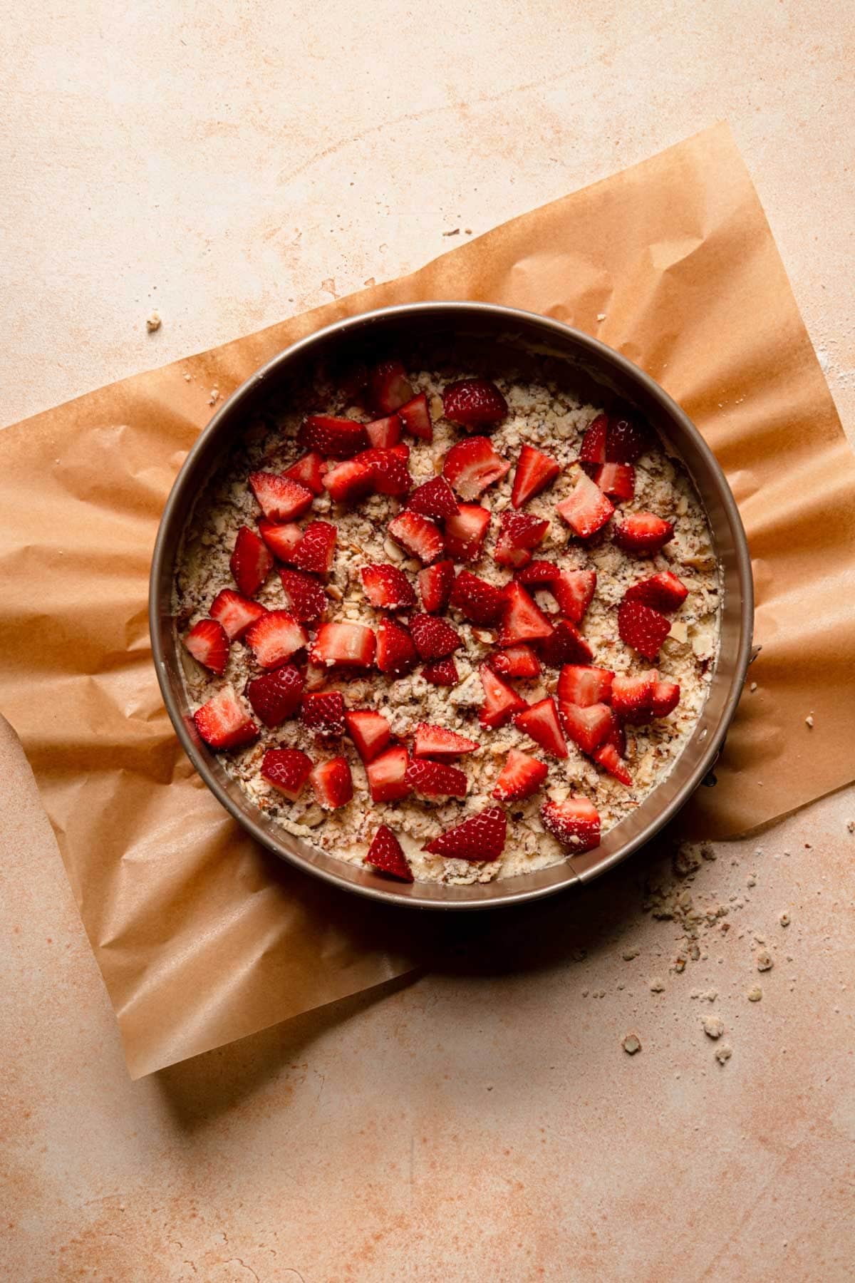 A pan with cake batter topped with crumble and strawberry pieces.