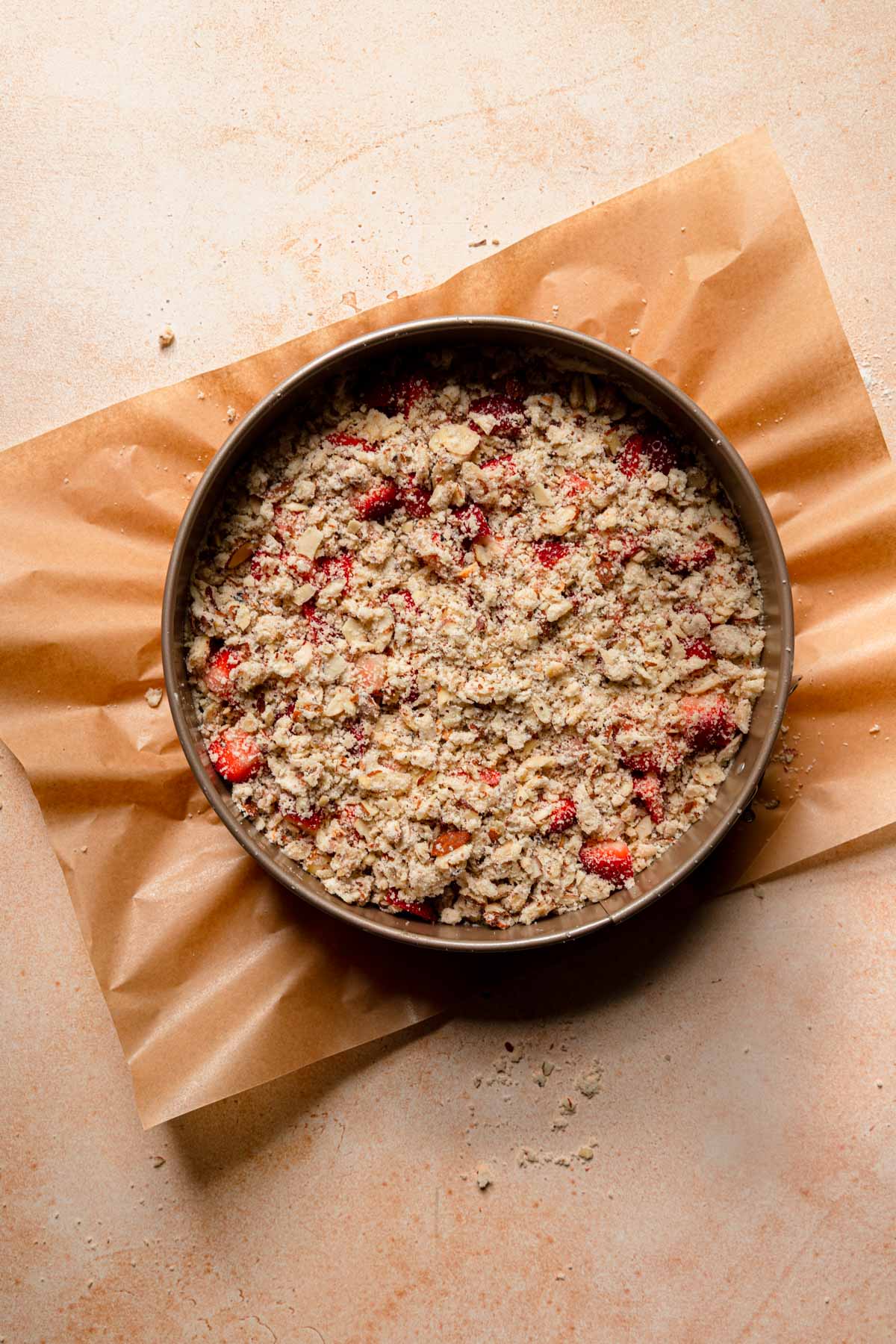A pan with cake batter topped with crumble and fresh strawberries.