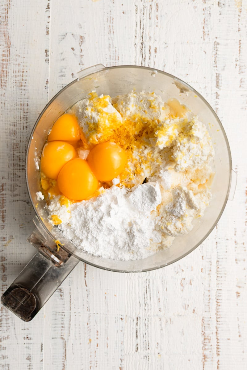 A food processor with cheese, eggs, powdered sugar and lemon zest.