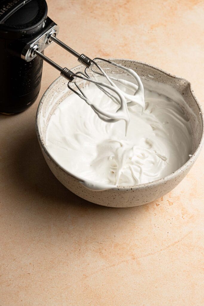 Stiff meringue in a bowl and a mixer.