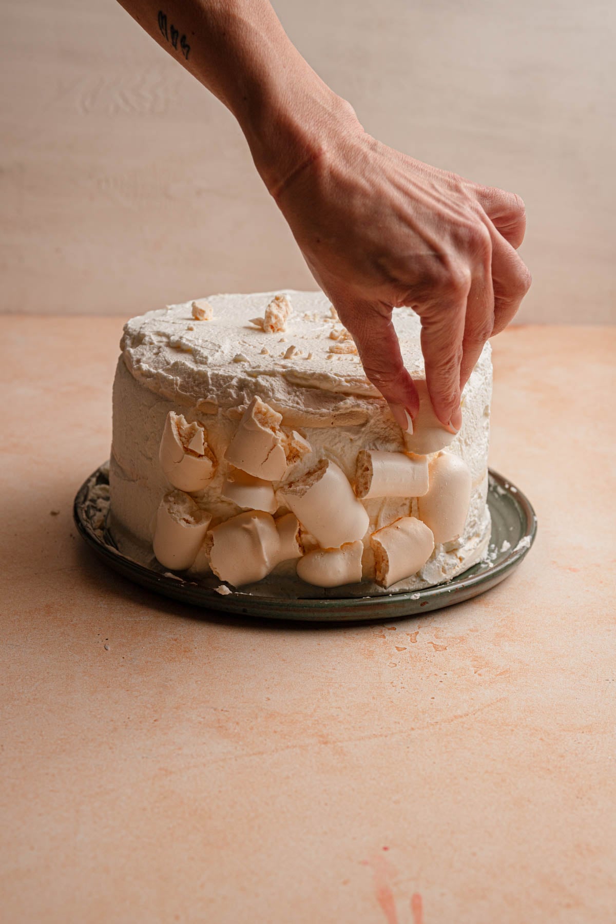 A hand sticking broken meringue pieces over a cake.