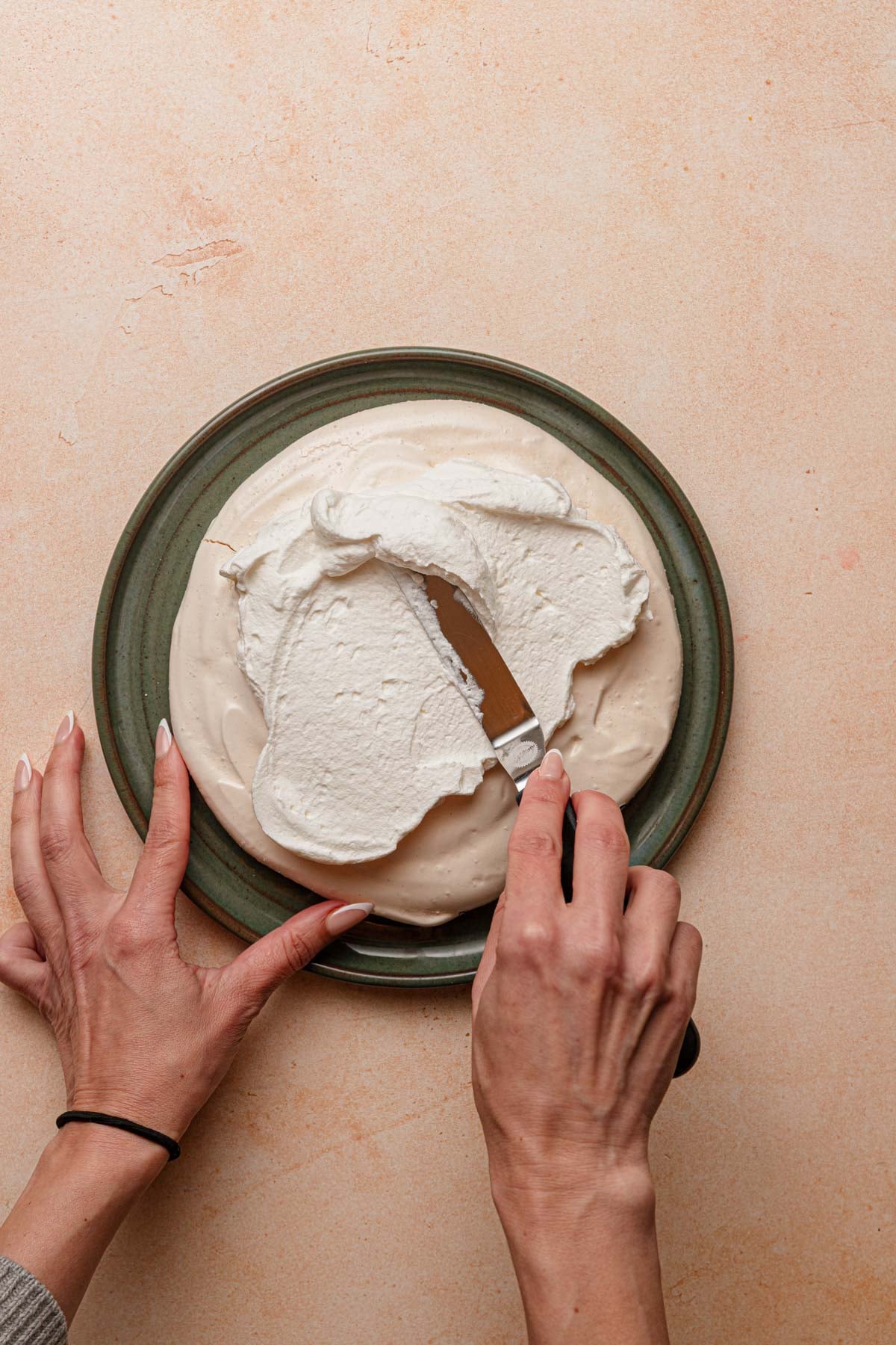 A hand spreading cream over a meringue disk.