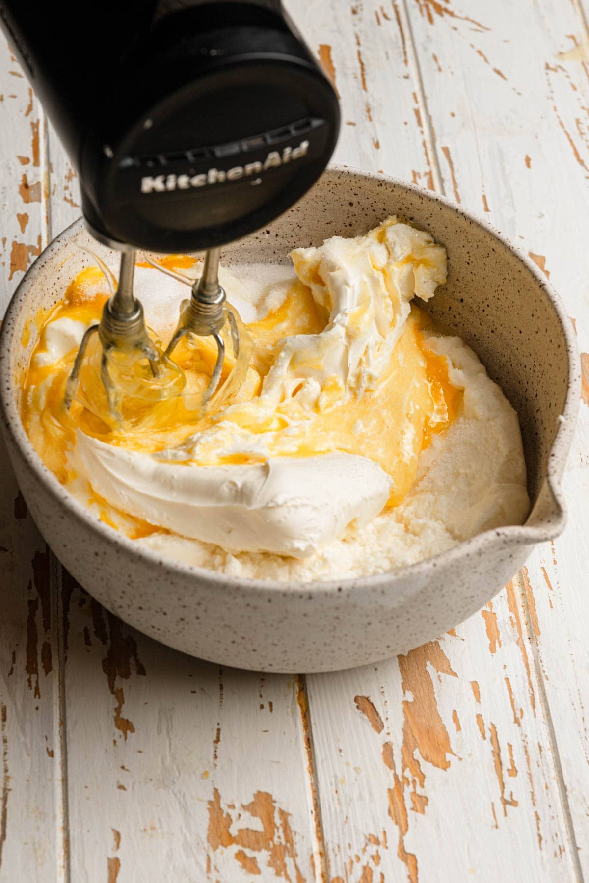 A hand mixer mixing cheese filling in a large bowl.