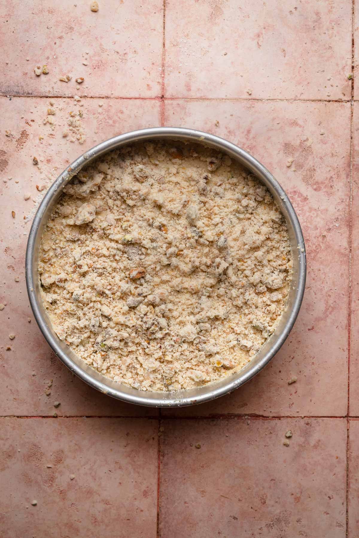 A pan with unbaked cake batter topped with pistachio streusel.