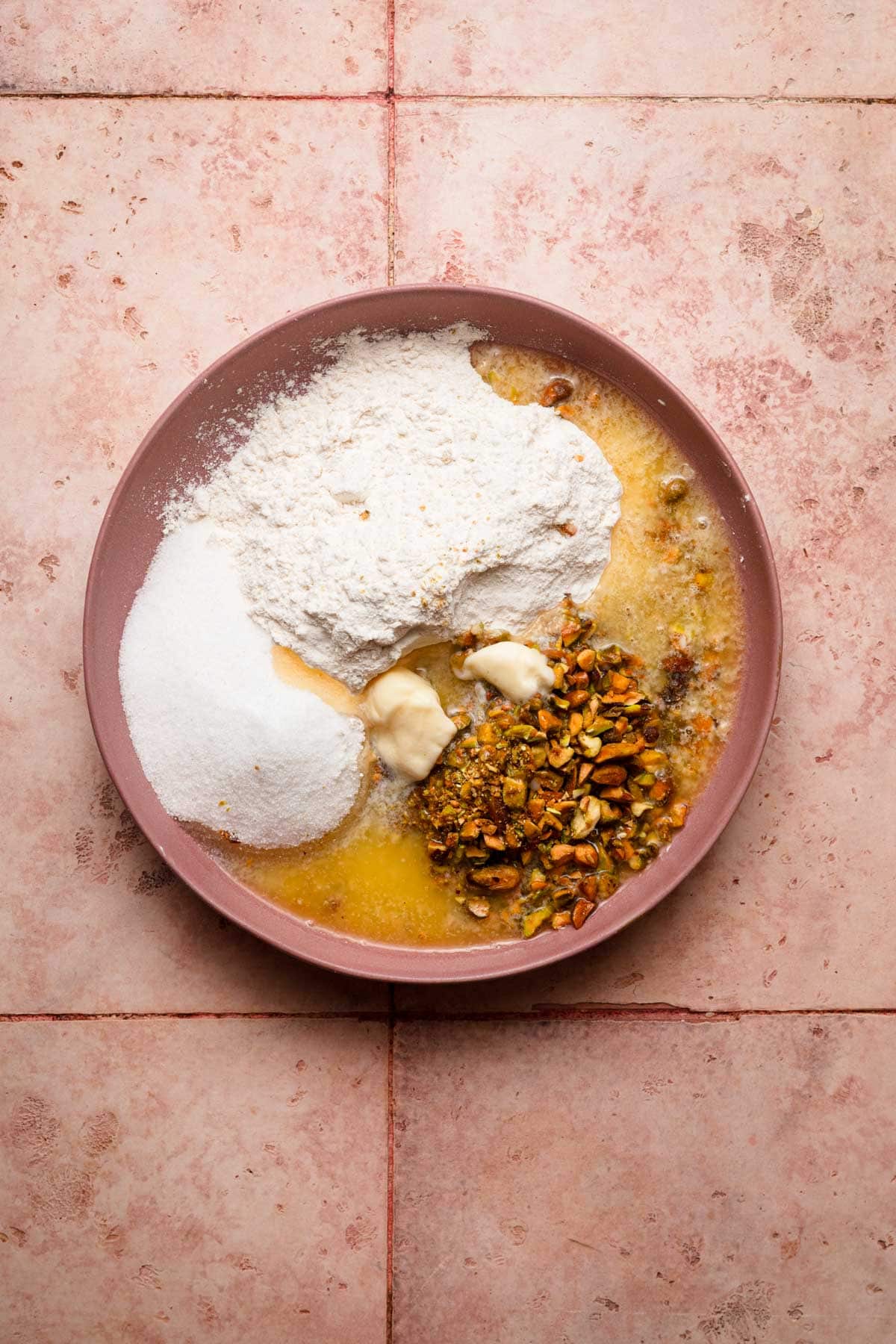 A bowl with flour, sugar, melted butter and chopped pistachios.