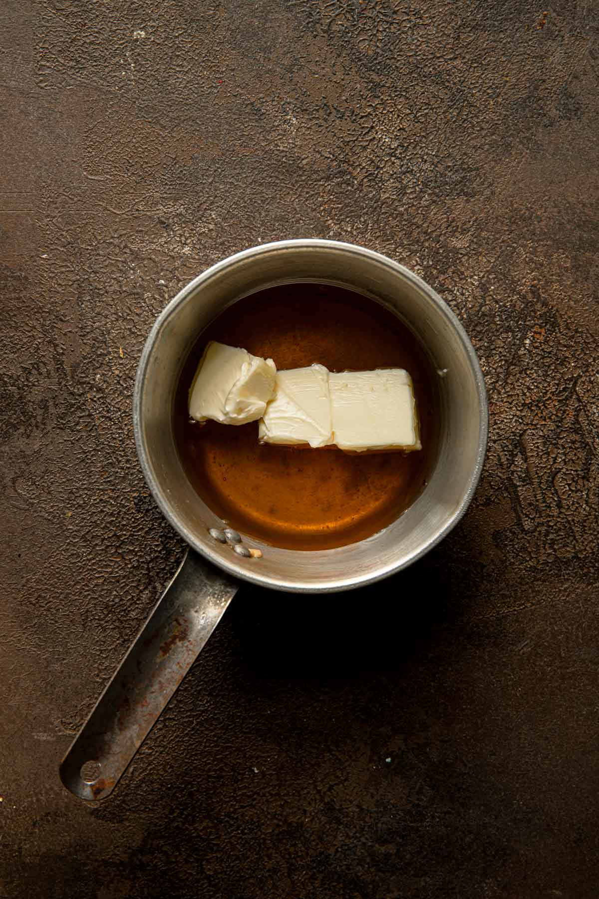 A sauce pan with honey and pieces of butter.