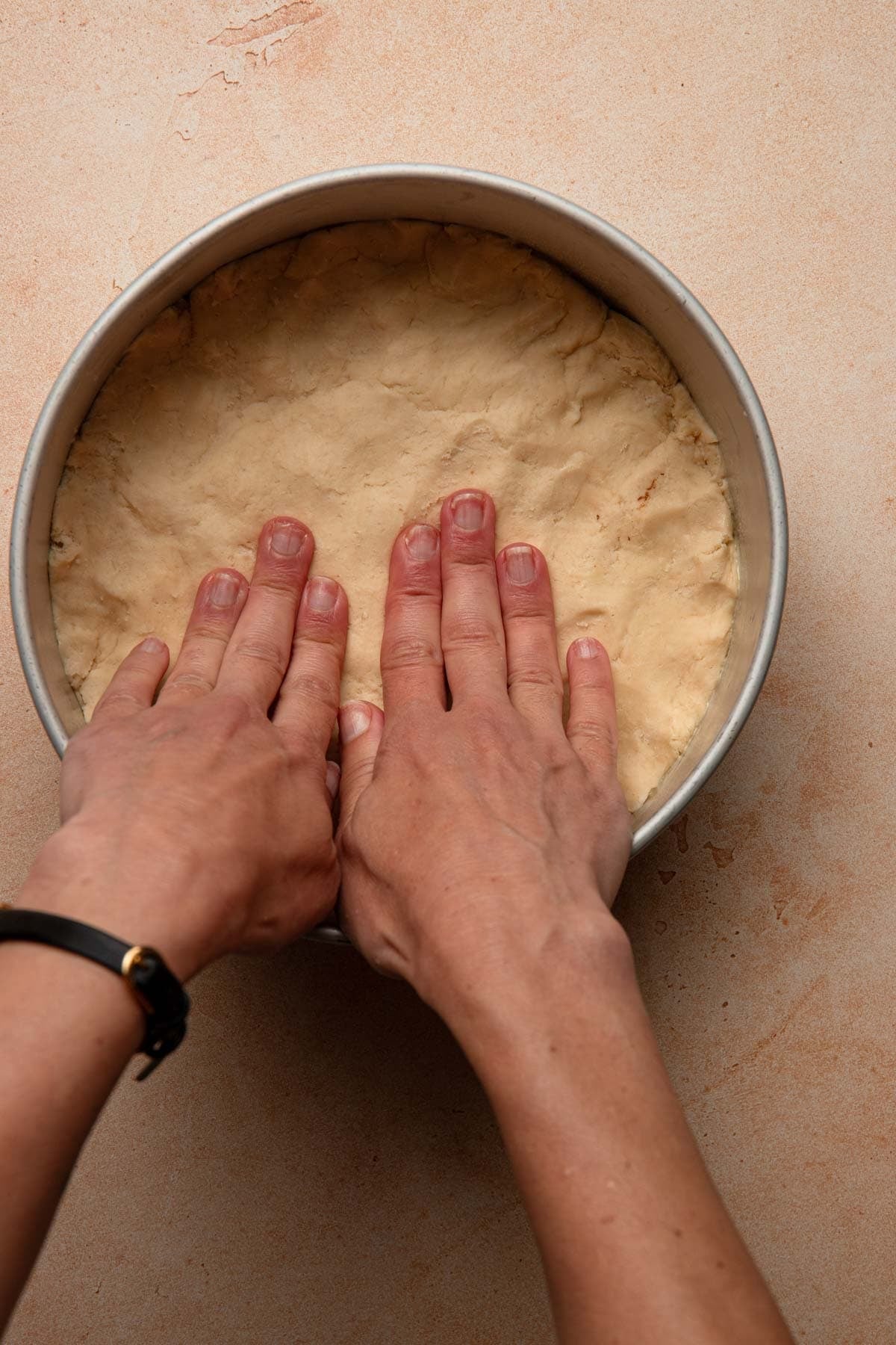 Hands pressing dough into a pan.