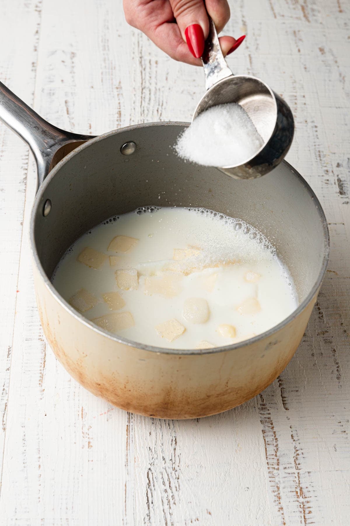 Adding sugar to a saucepan with milk and butter.