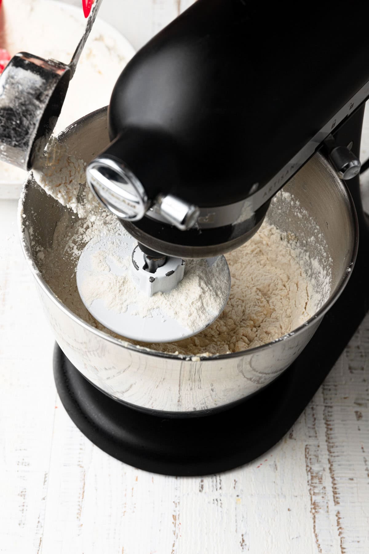 Adding flour to a mixing bowl attached with the dough hook.