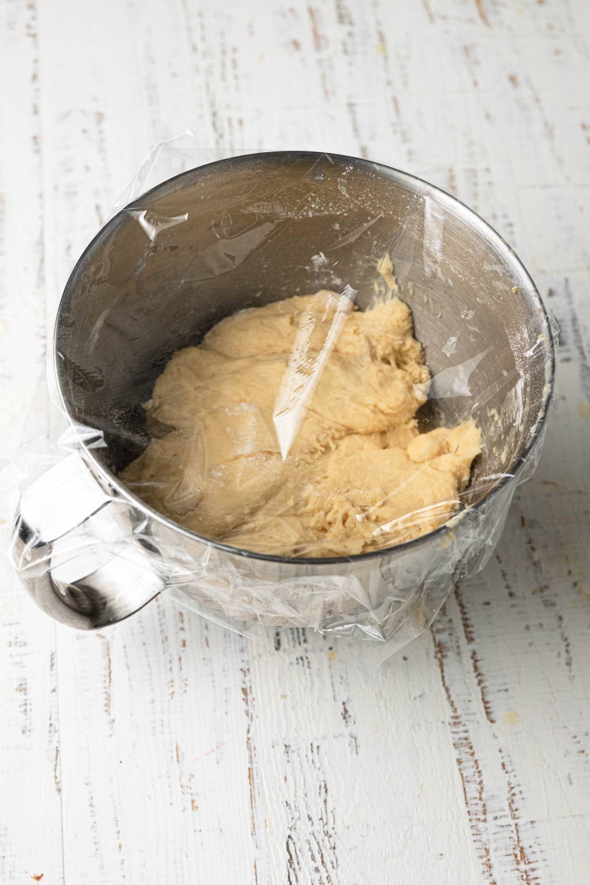 A mixing bowl with dough covered with plastic wrap.