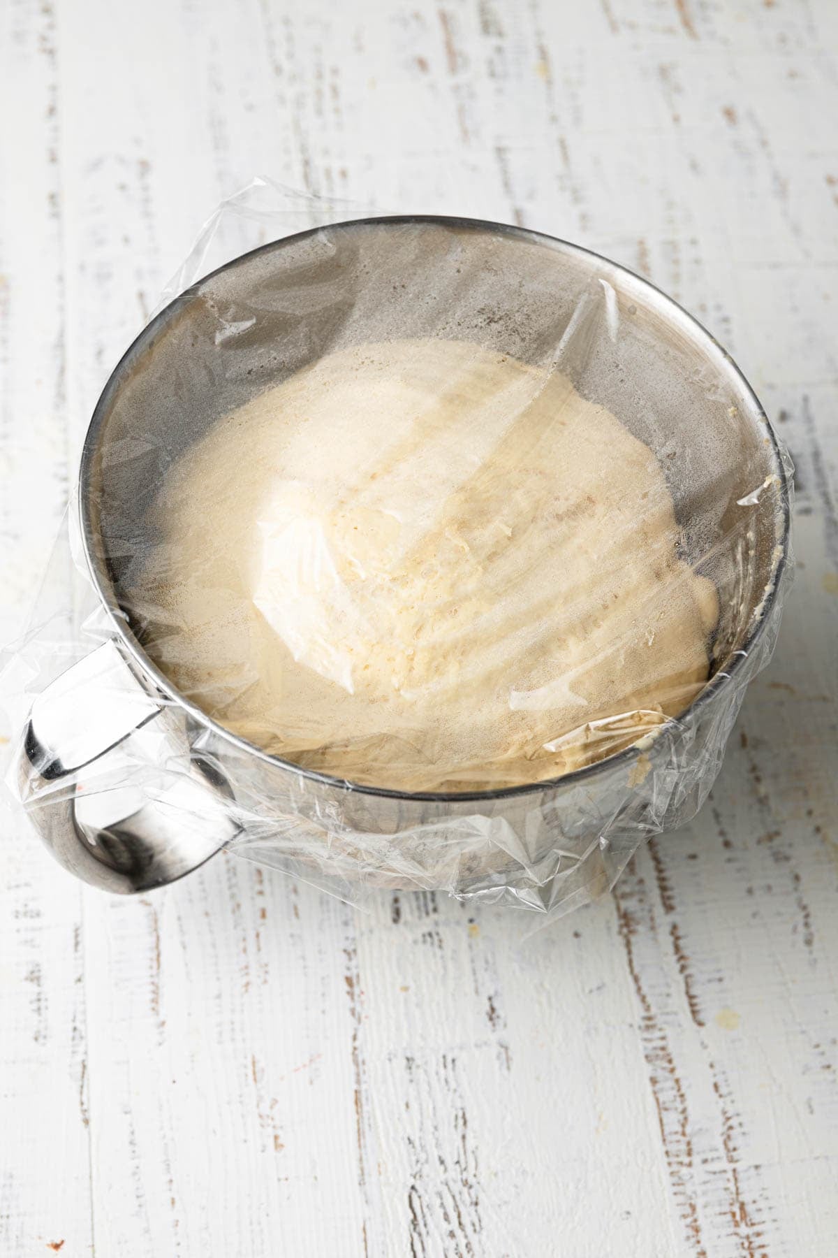 A mixing bowl with proofed dough covered with plastic wrap.