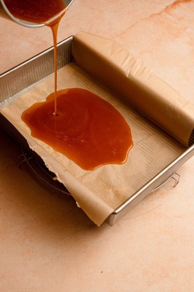 Pouring golden sauce into a brown pan lined with parchment paper.