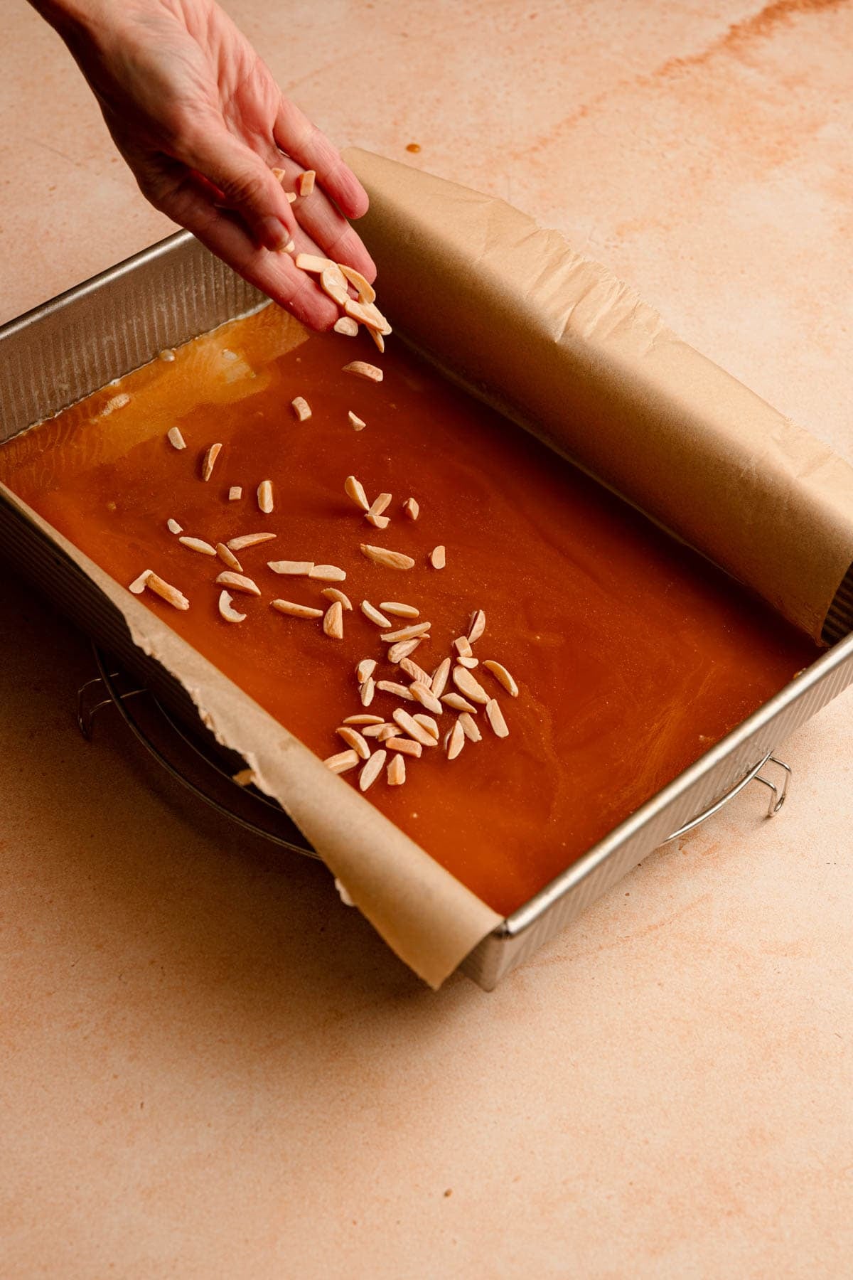 Sprinkling chopped nuts over a pan lined with parchment paper and topped with honey syrup.