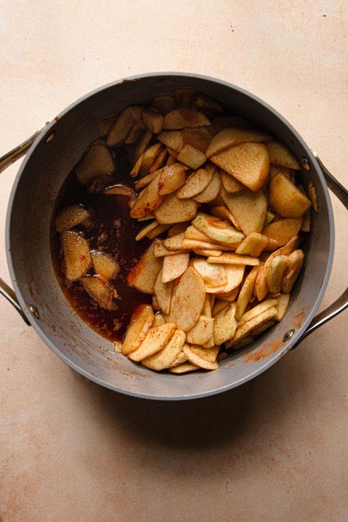 A pot with sliced apples tossed in cinnamon and sugar and the juices of the apples on the sides of the pan.