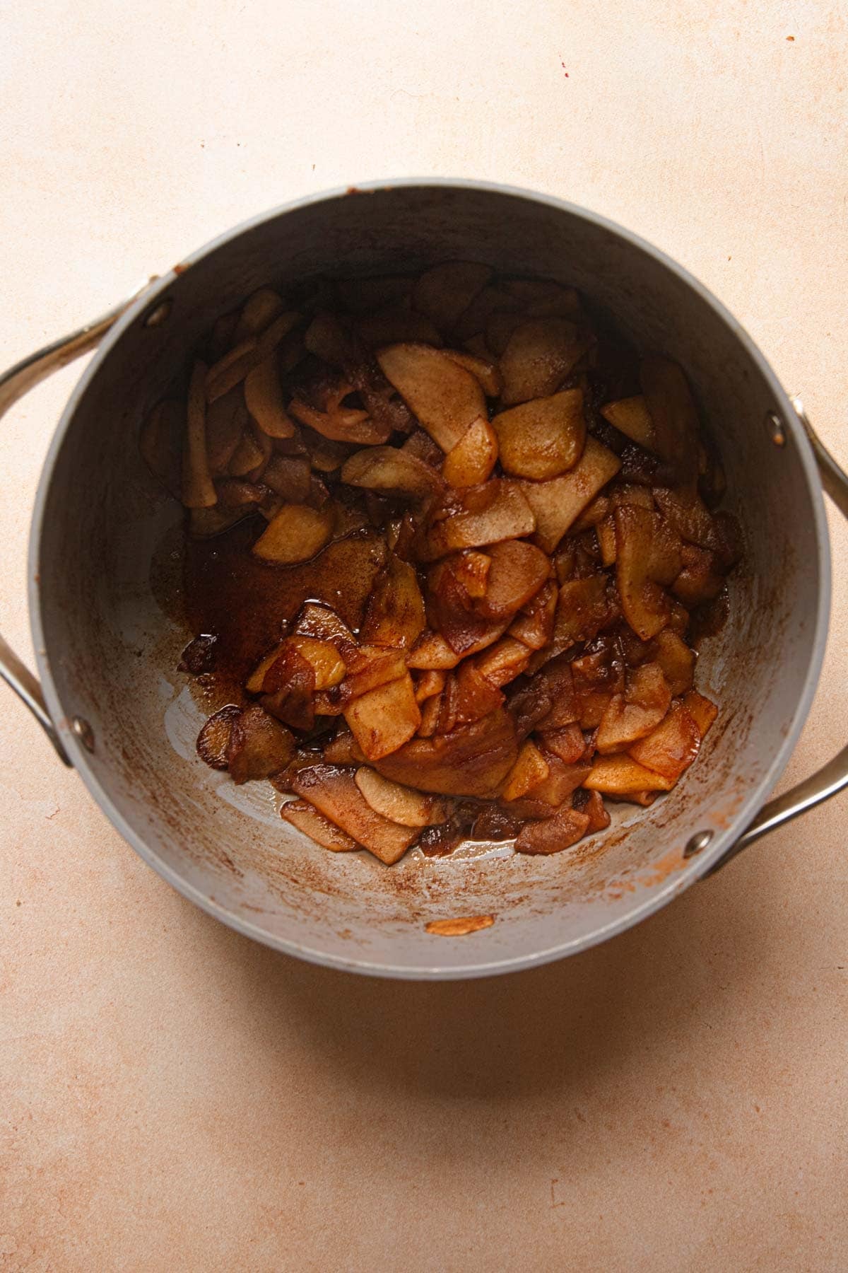A pot with cooked apples slices and cinnamon.