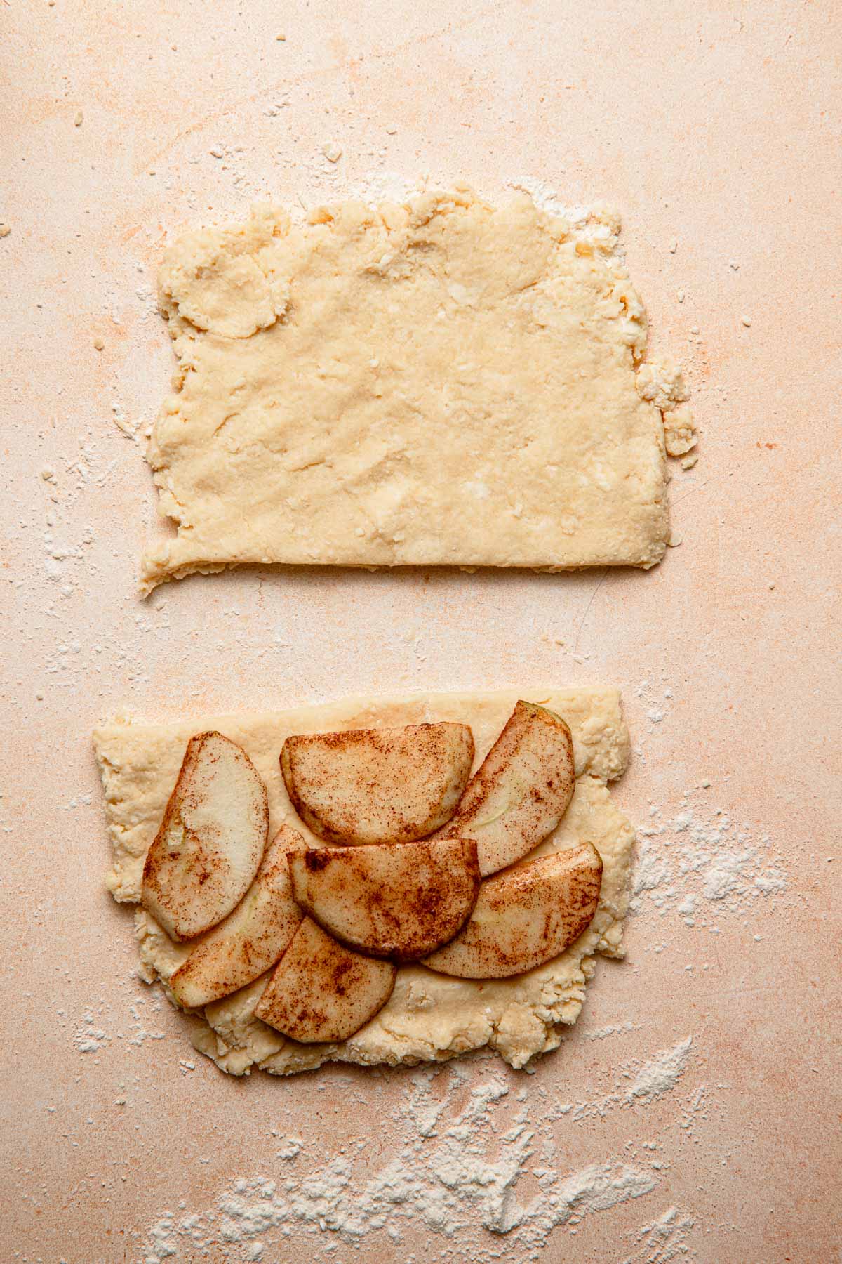Scone dough pressed into two parts. the bottom one topped with apple slices/