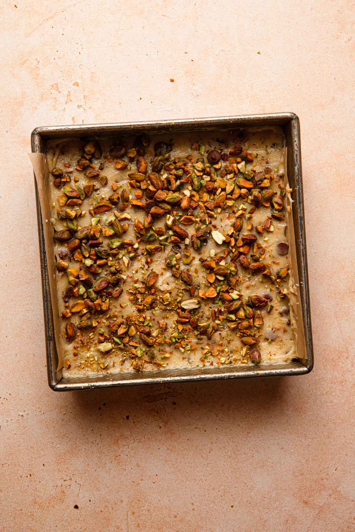 Blondie batter in a pan topped with chopped pistachios.