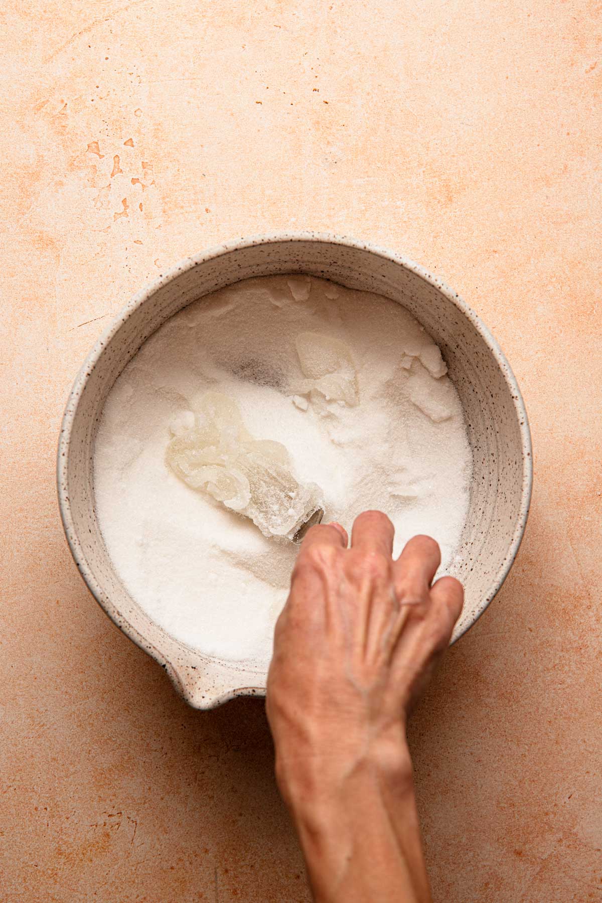 A hand mixing sugar with corn syrup into sugar using a fork.